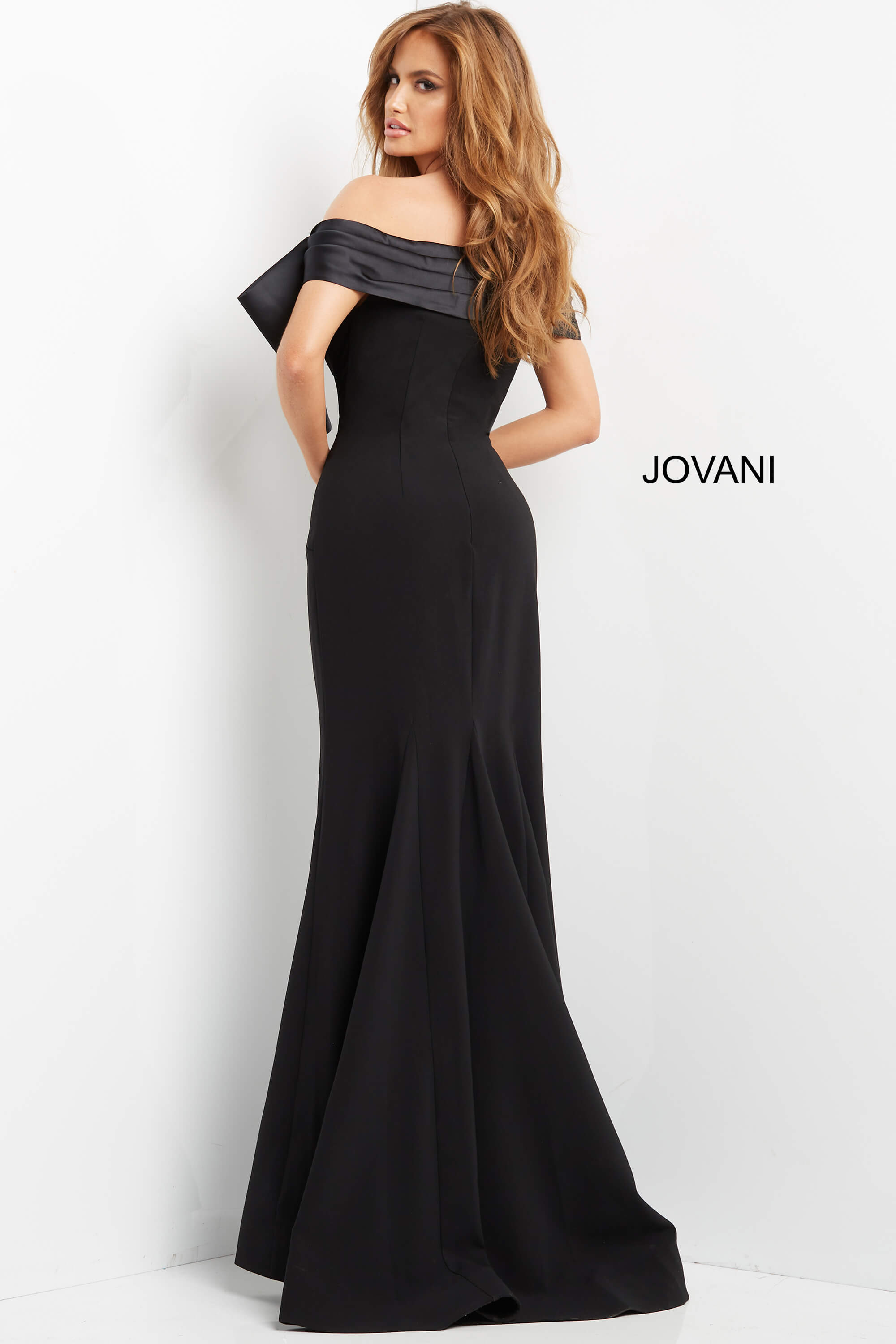 Model wearing Jovani 07014 black off-the-shoulder gown with large bow, back view.