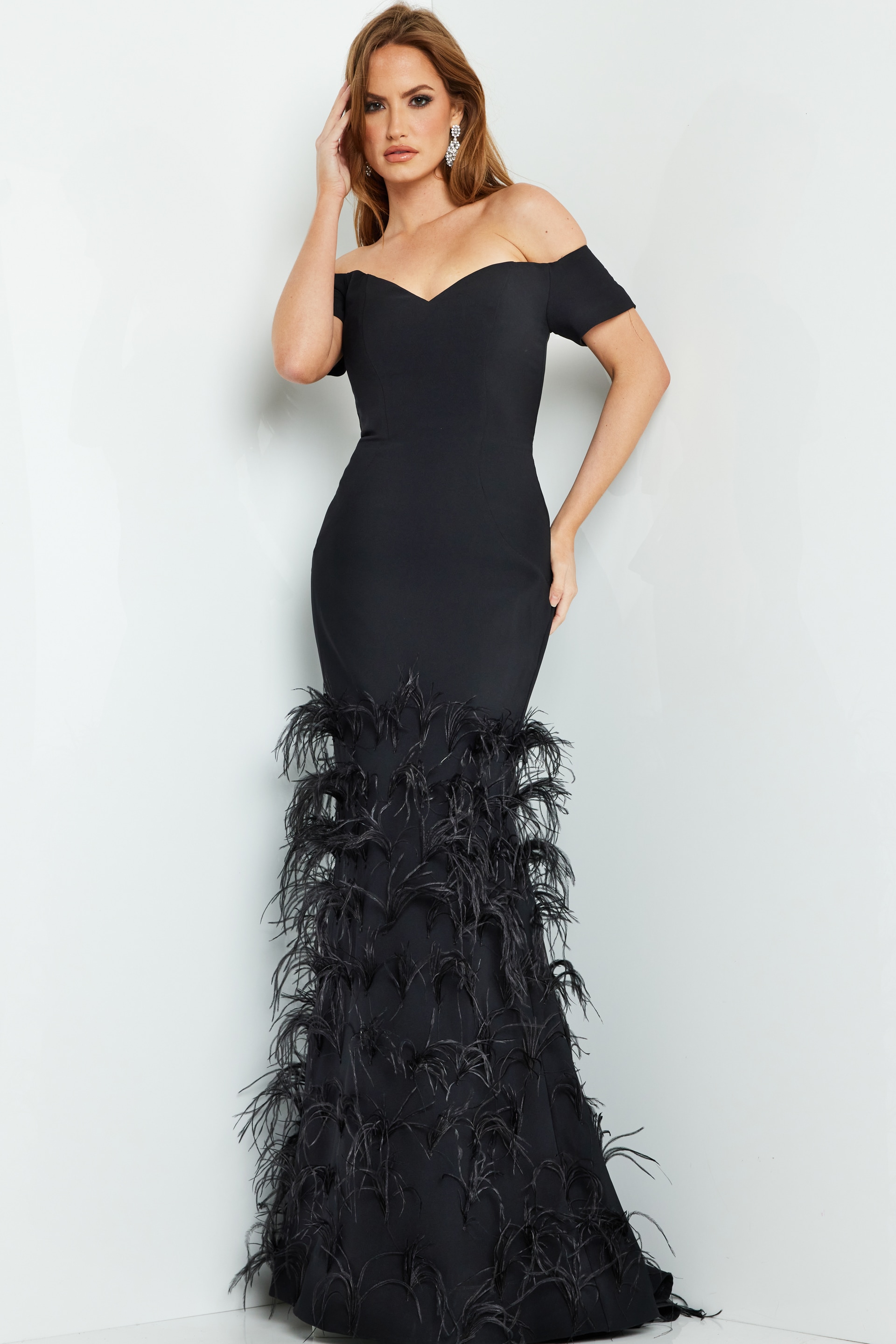 Model wearing Jovani 08384 black off-the-shoulder mermaid gown with feather details.