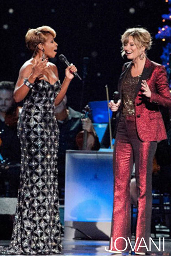 Model wearing Jovani 79121 black gown with another person in a red suit.
