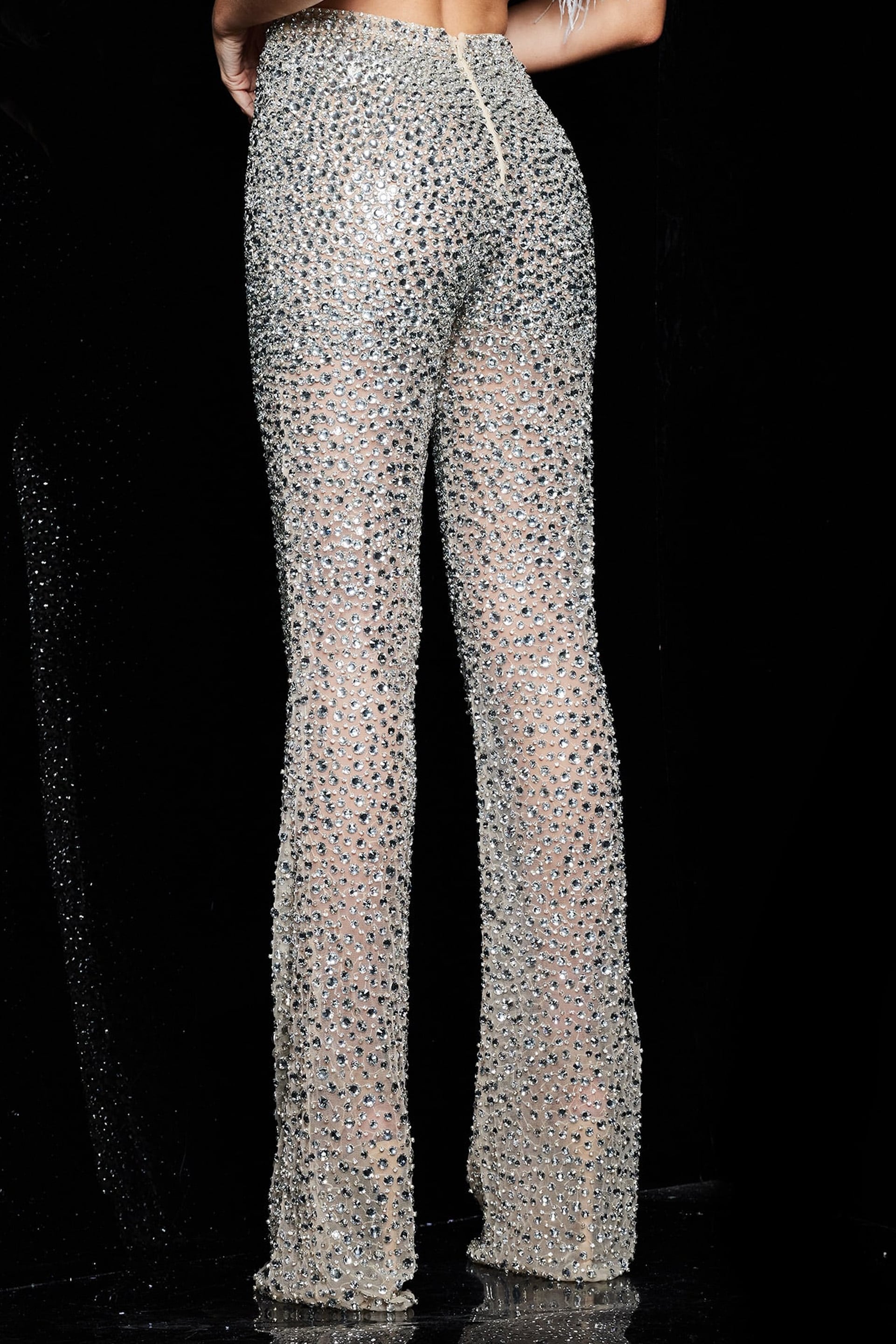 Model wearing Jovani 22781 featuring embellished nude pants and feather detailed top, back view.