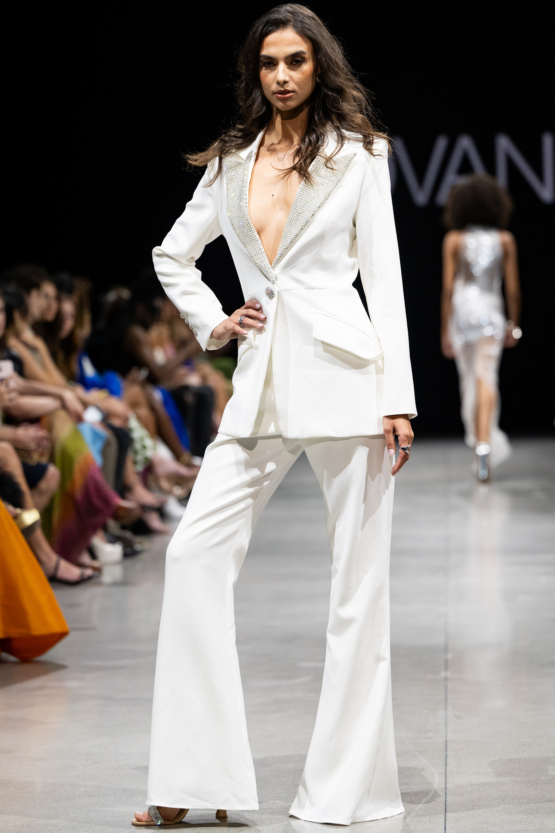 Model wearing Jovani 23336 white suit with embellished lapel and wide-leg pants.