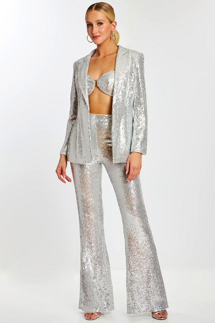 Model wearing silver sequin pantsuit with flared trousers, bralette top, and open blazer.