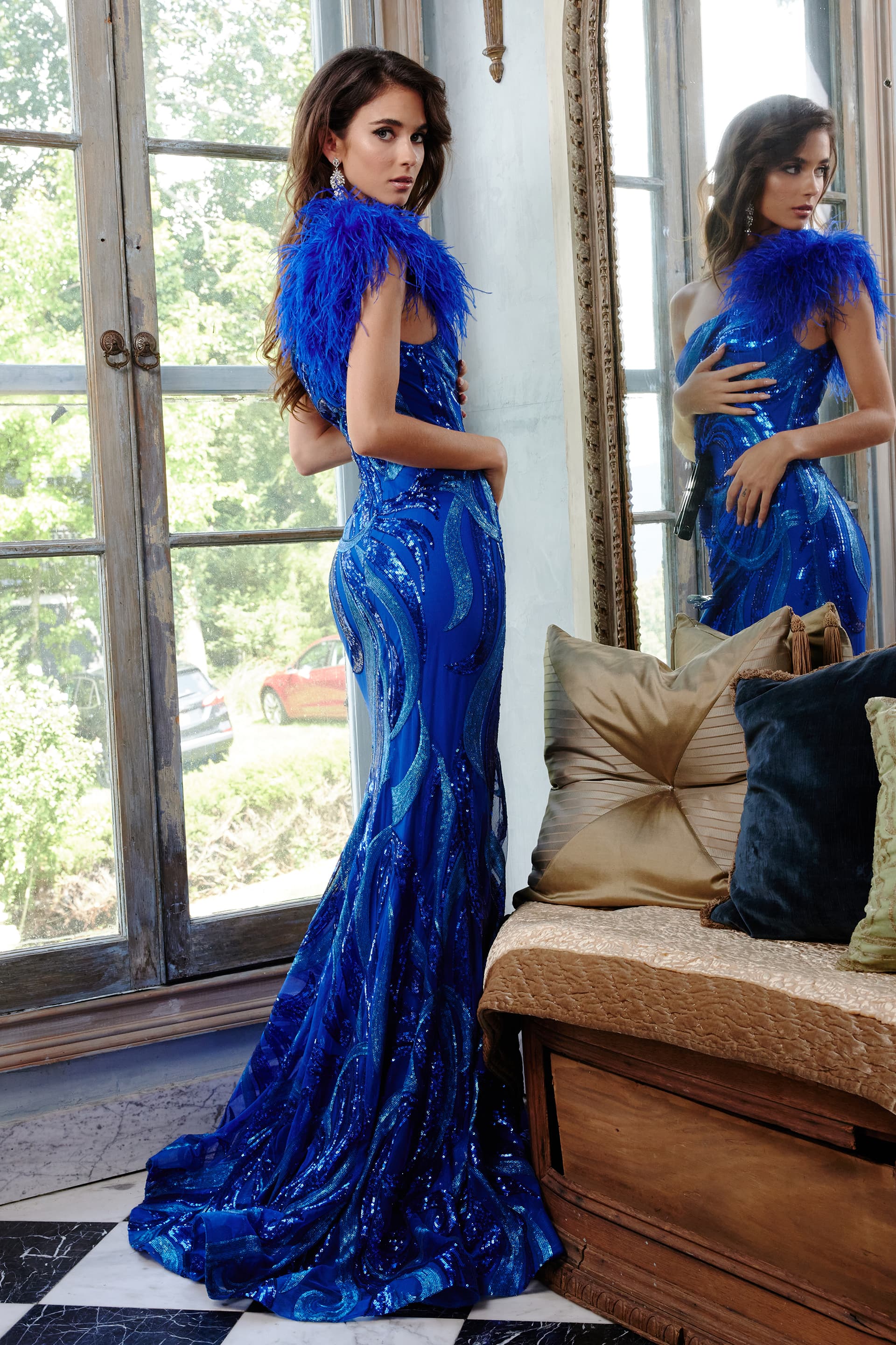 Model wearing Jovani 32596 royal blue gown with feather detail at shoulder, back view.