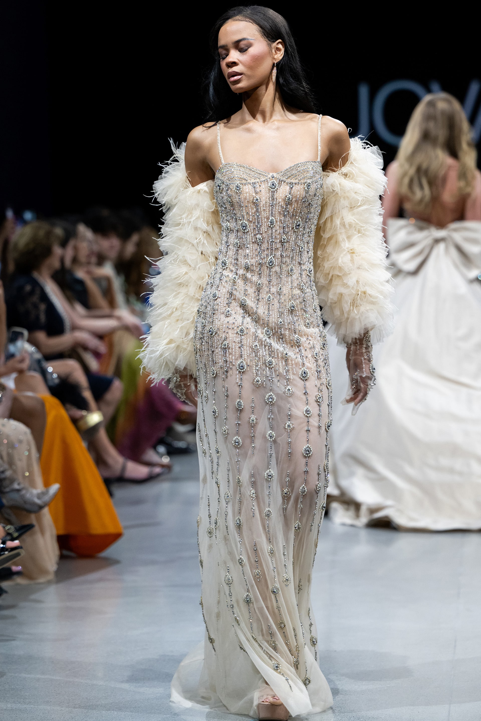 Model wearing Jovani 36510 nude dress with intricate beadwork and off-shoulder cape sleeves, showcasing front view.