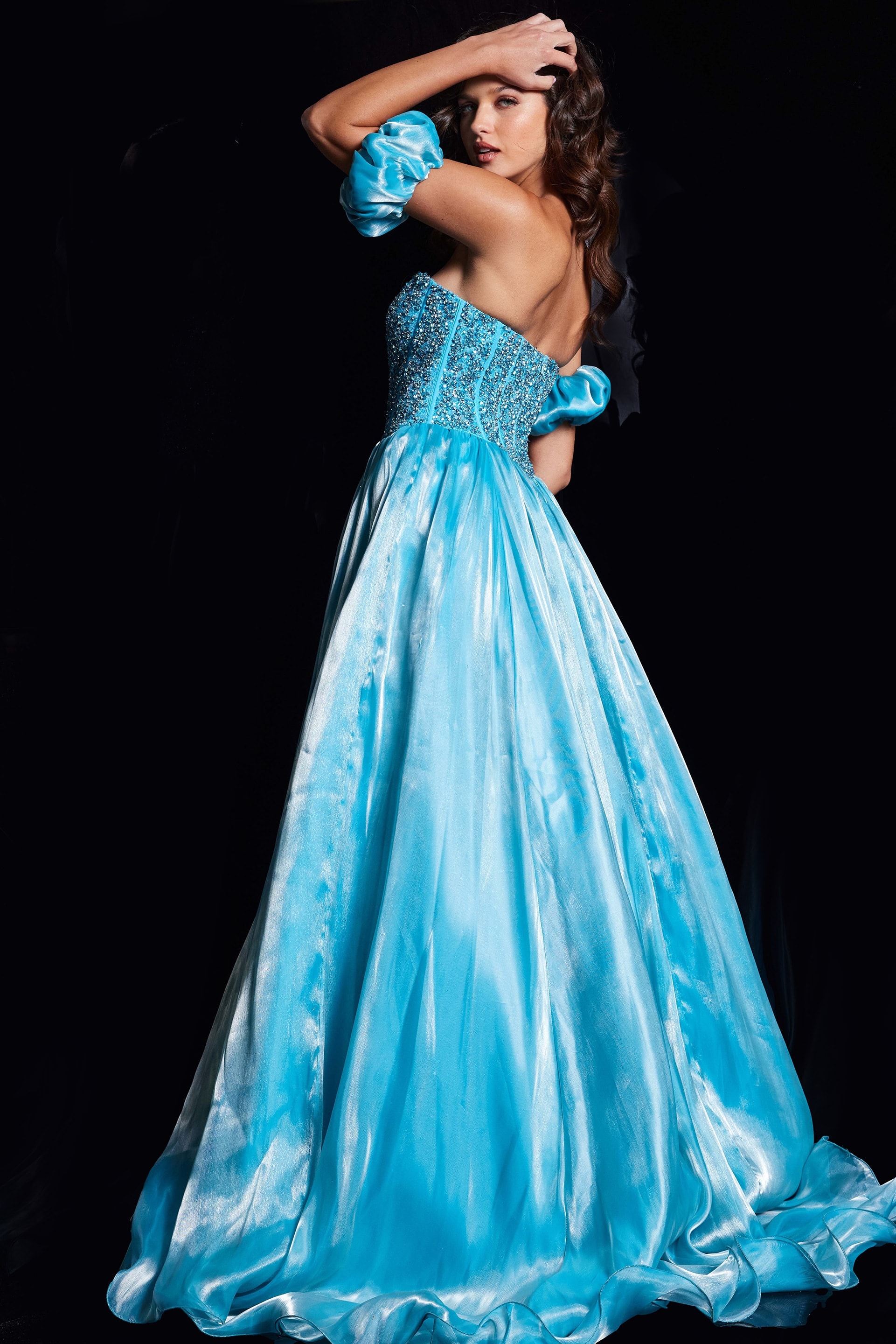 Model wearing Jovani 36591 blue ball gown showcasing the back with off-the-shoulder puff sleeves and flowing skirt.