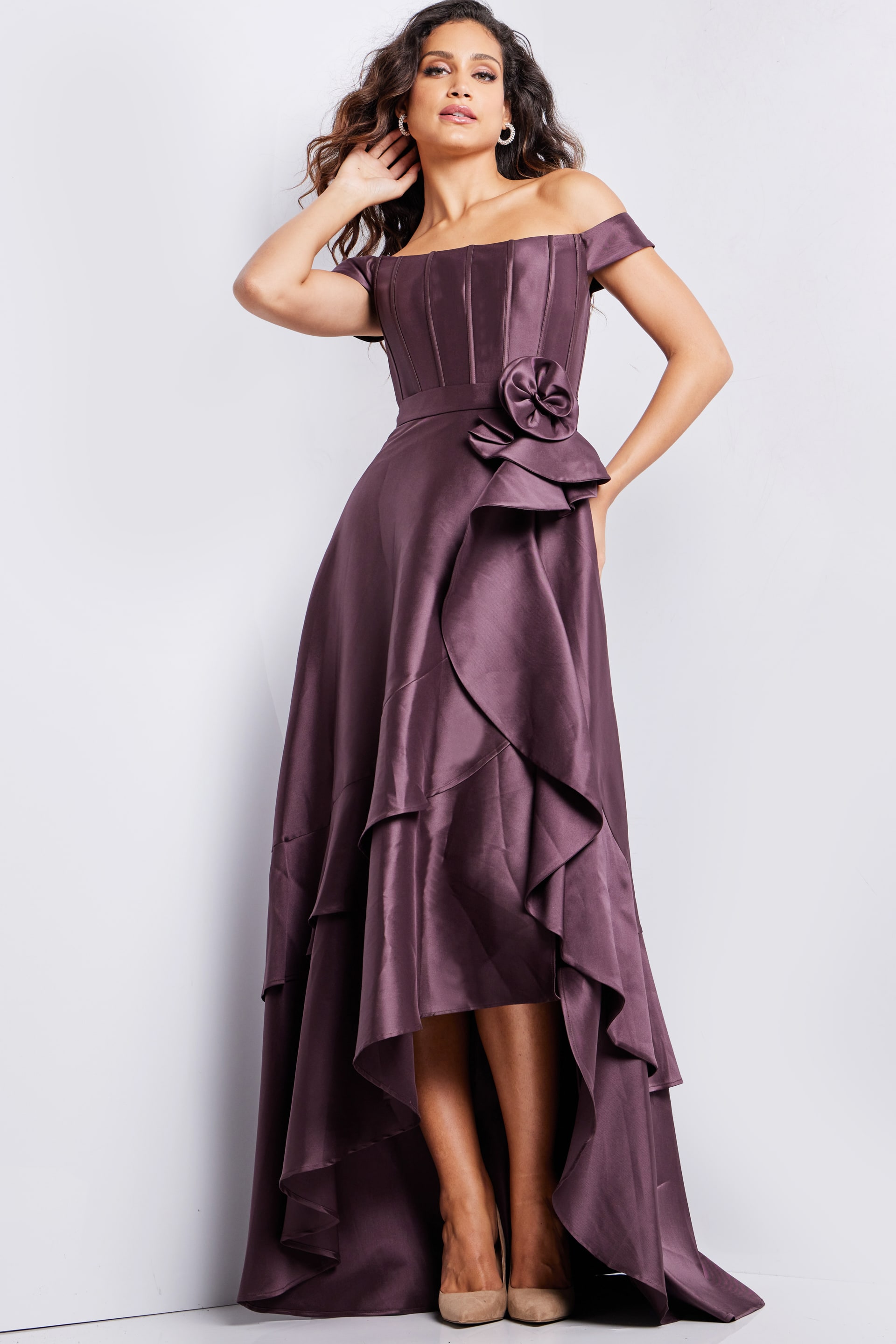 Model wearing Jovani 37014 brown dress with off-shoulder neckline and rosette detail at waist.