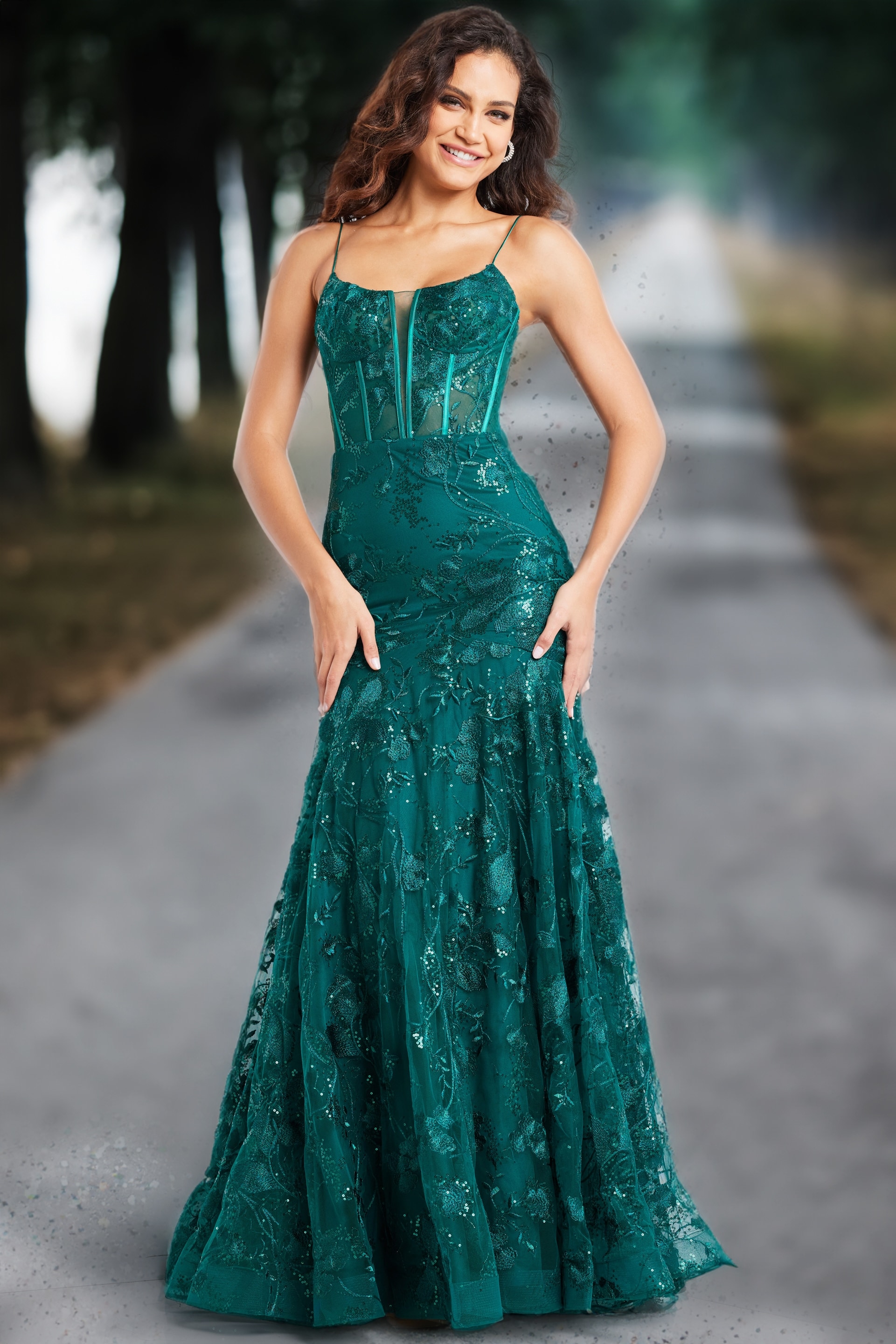 Model wearing Jovani 38004 dark green gown with elegant floral design, street view.