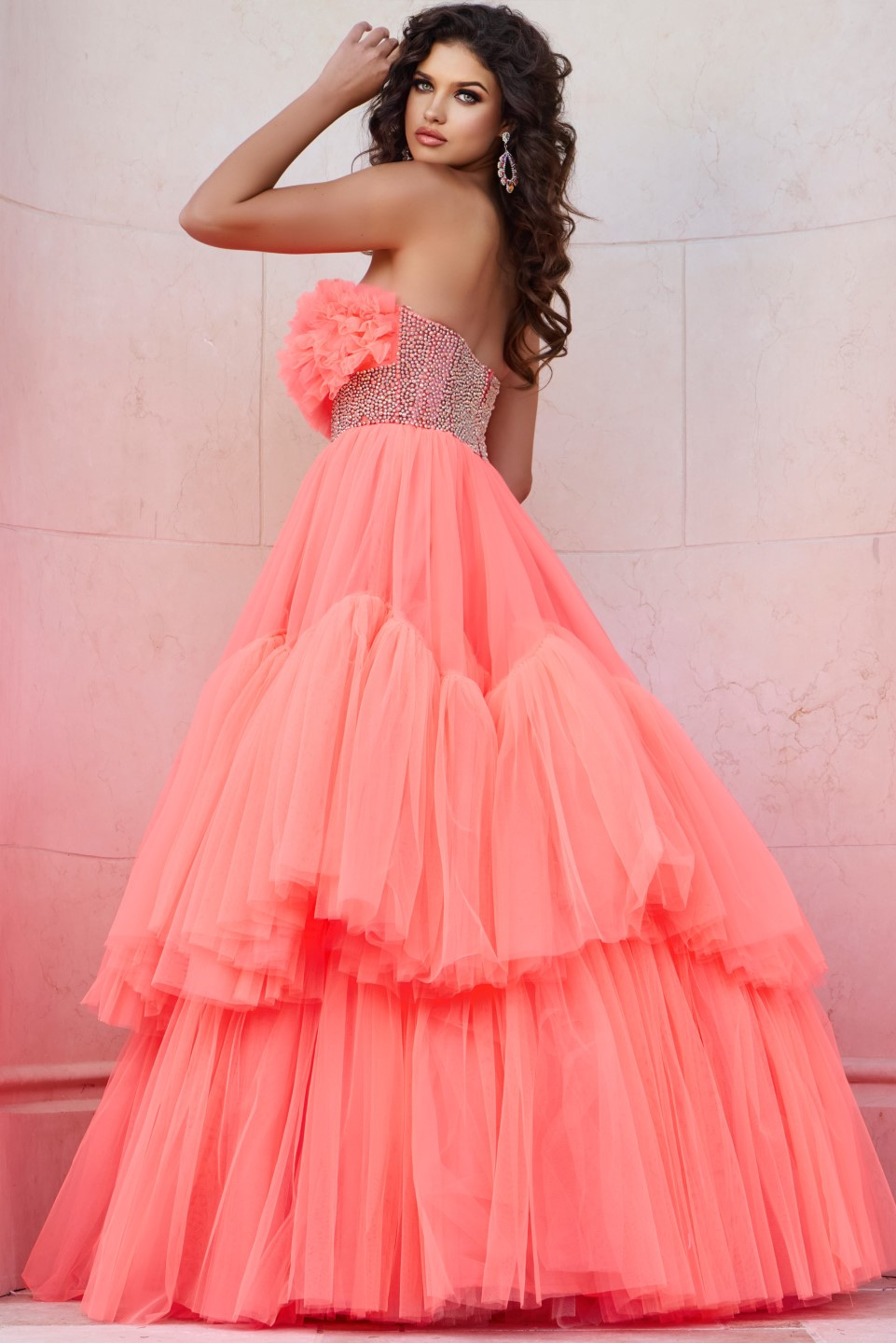 Model wearing Jovani 38299 orange gown with floral ruffles and embellished waist, side view.