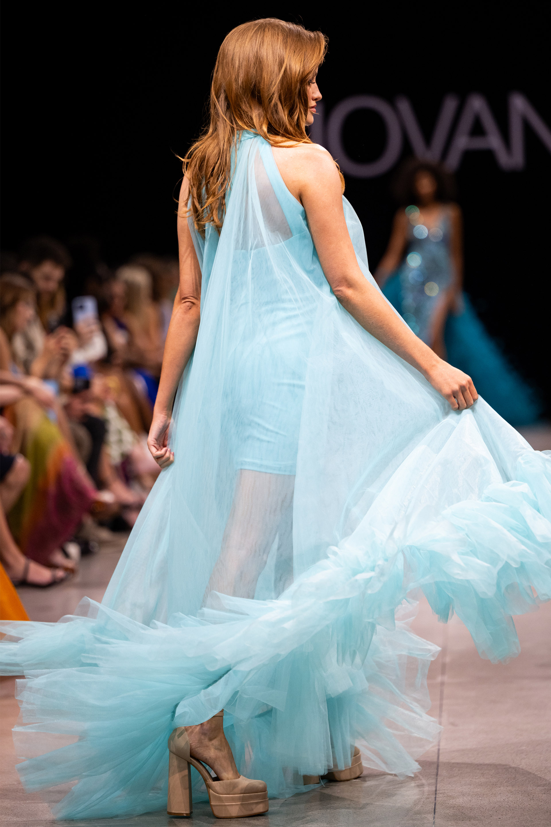 model wearing Jovani 38720 blue dress with high neckline and flowing layers from the back view