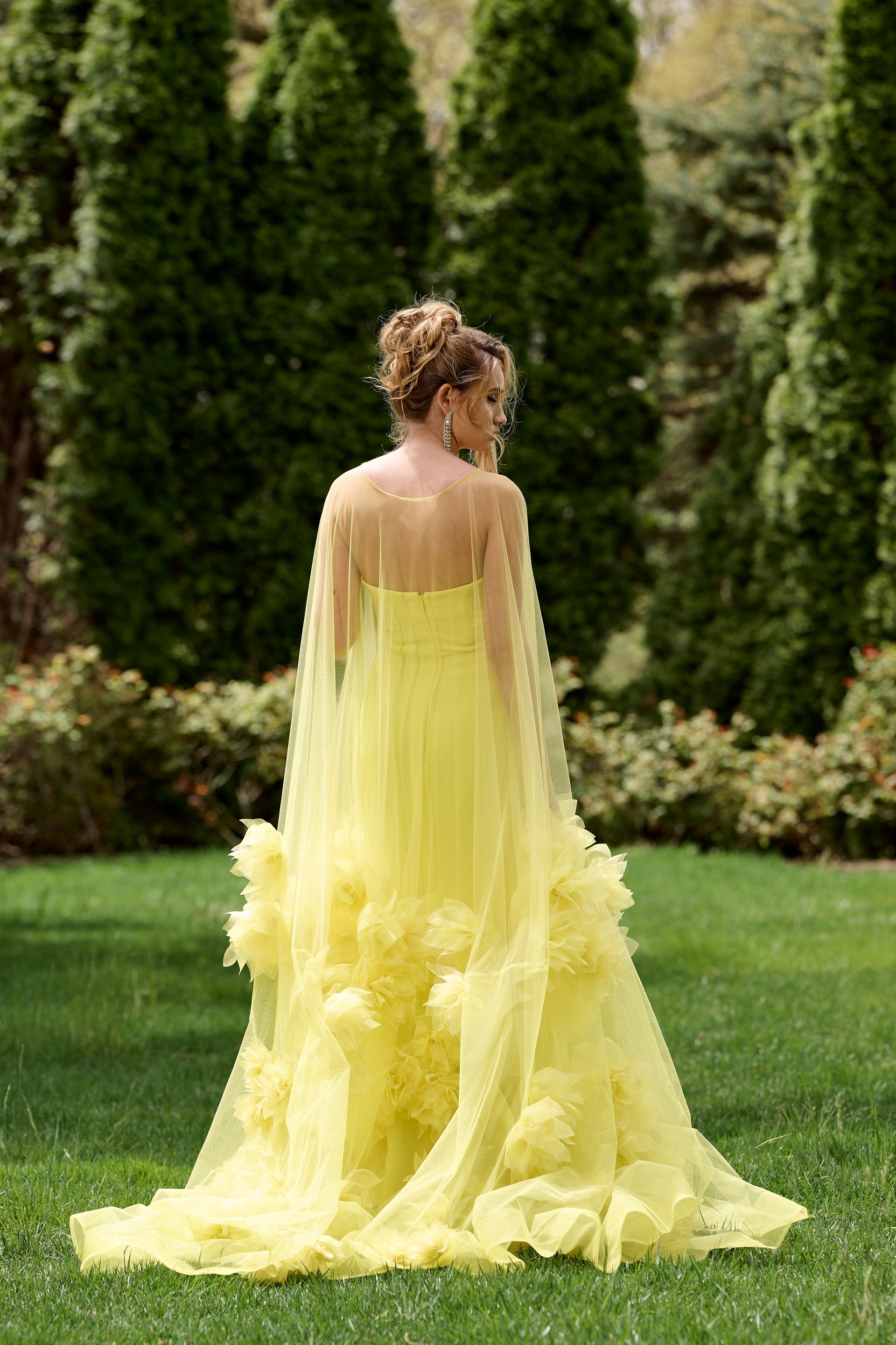Model wearing Jovani 40092 yellow gown with floral appliqués, back view