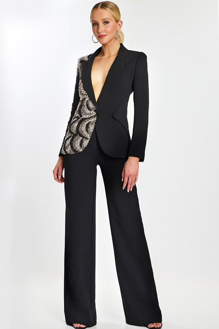 Model wearing black pantsuit with asymmetric sequin detailing and plunging neckline.