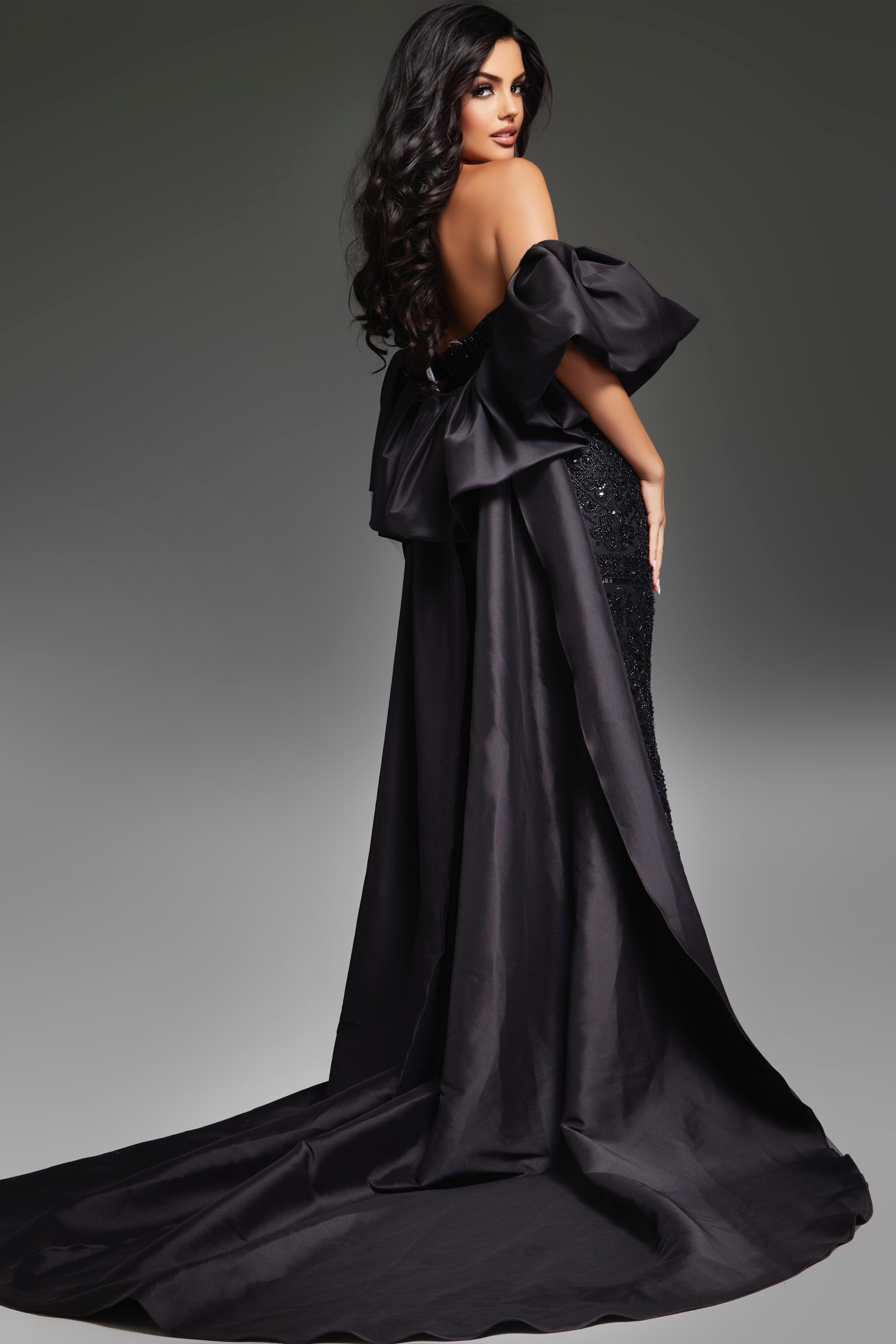 Model wearing Jovani 42137 black evening gown, back view with draped overskirt