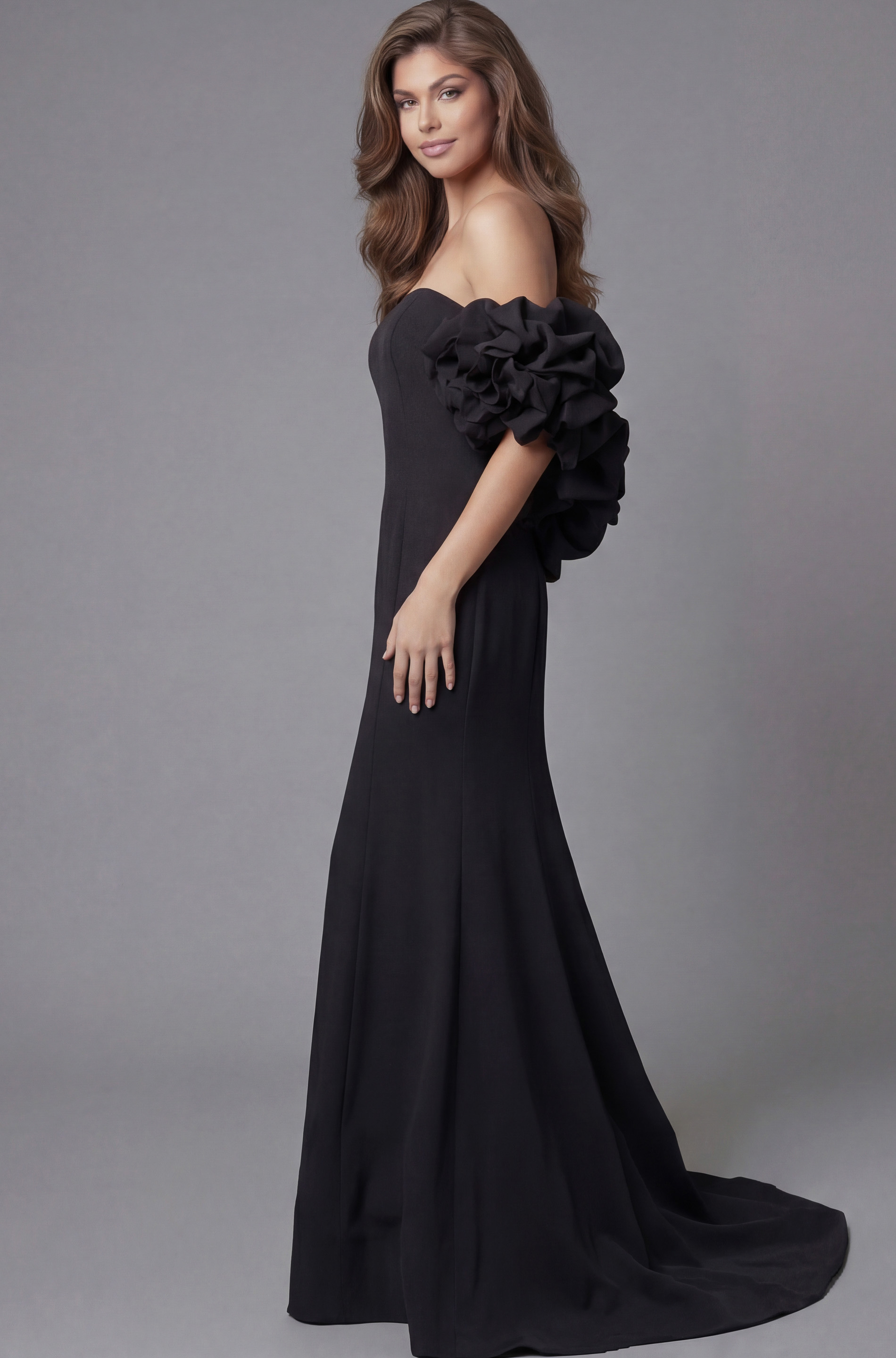 Side profile of Jovani 45653 black off-the-shoulder mermaid gown highlighting the dramatic rosette ruffle sleeve detail, clean bodice, and flowing train.