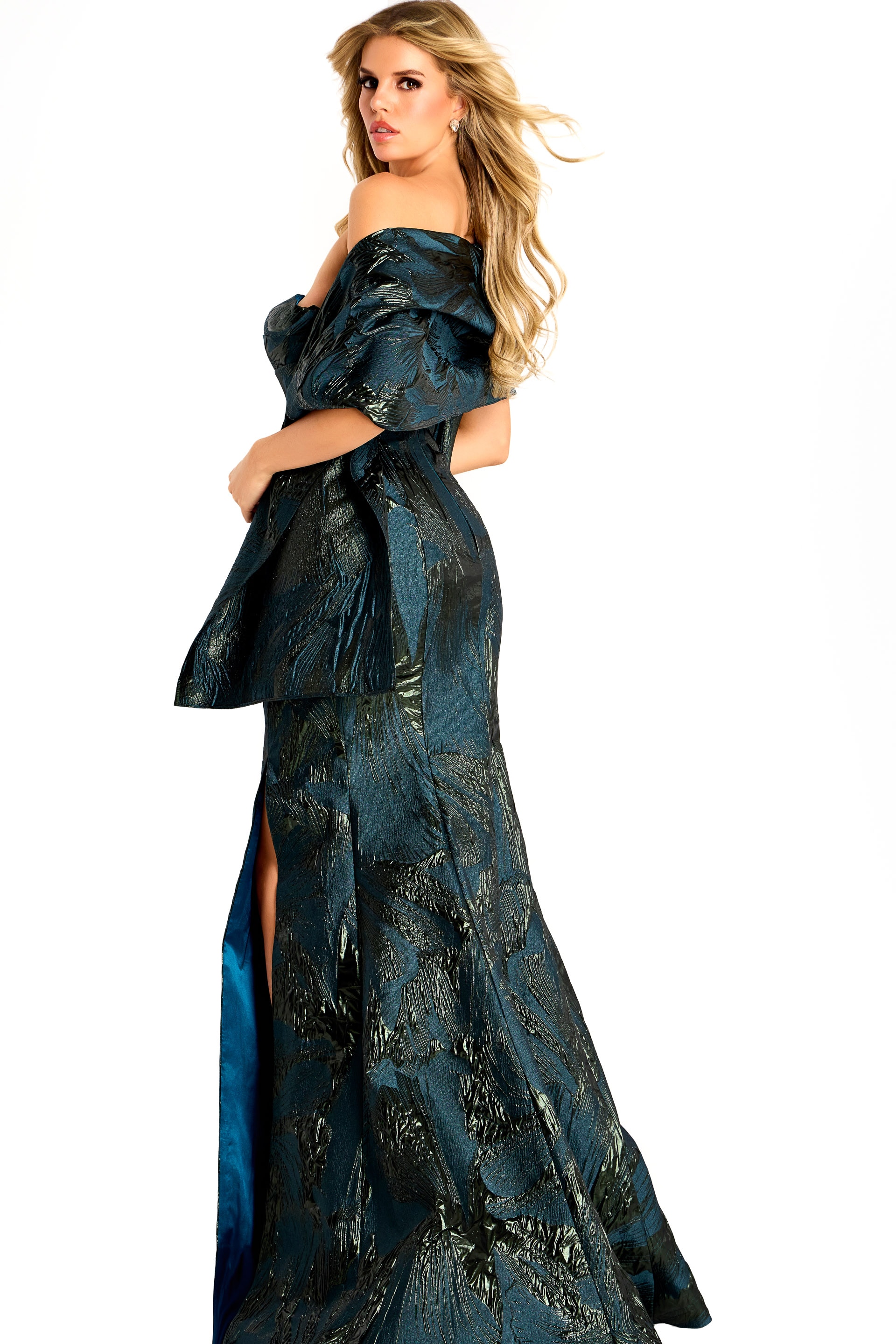 Off-shoulder metallic jacquard gown with structured draped sleeves, fitted bodice, and a floor-length slit skirt.