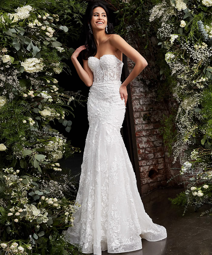 Model wearing JB02836 elegant white gown with lace appliqués, front view, surrounded by flowers