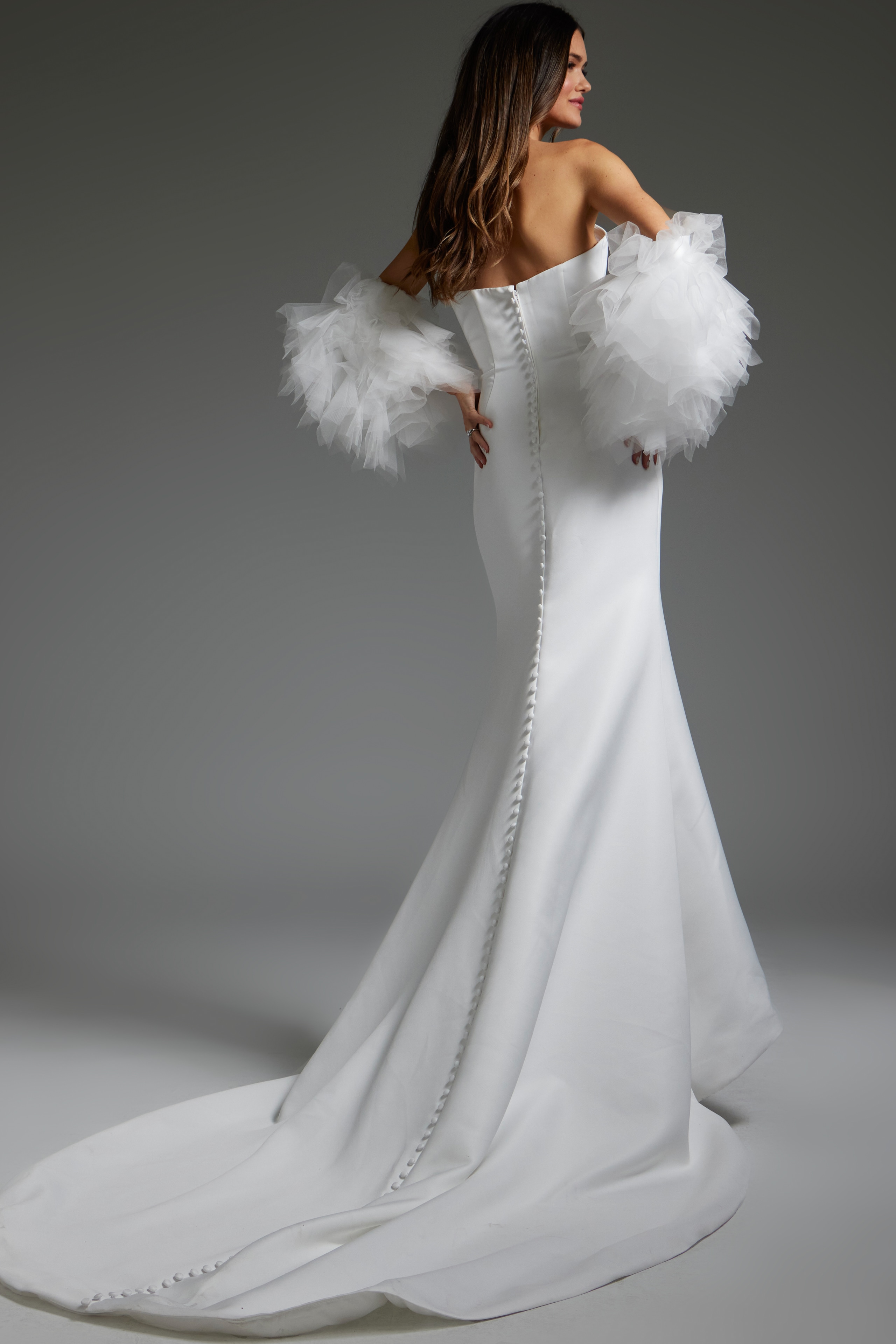 Back view of model in Jovani JB40601, white mermaid gown with button detail.