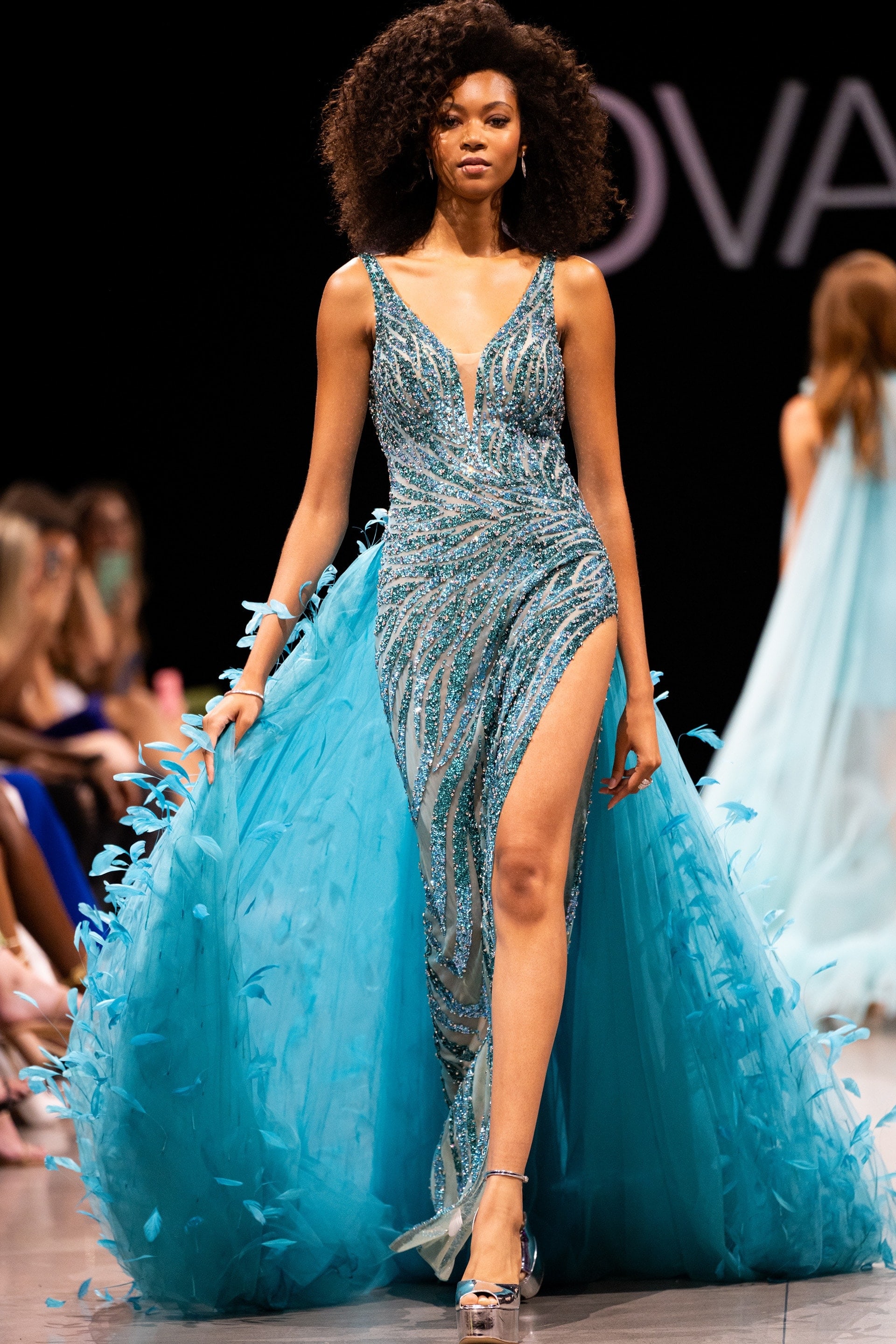 Model wearing Jovani S23074 blue gown with feather-like back details.