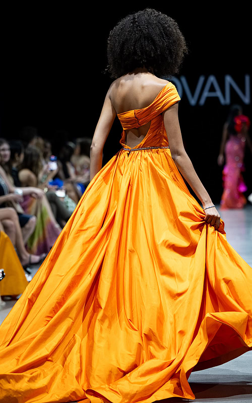 Back view of model wearing S38441 orange gown with flowing skirt